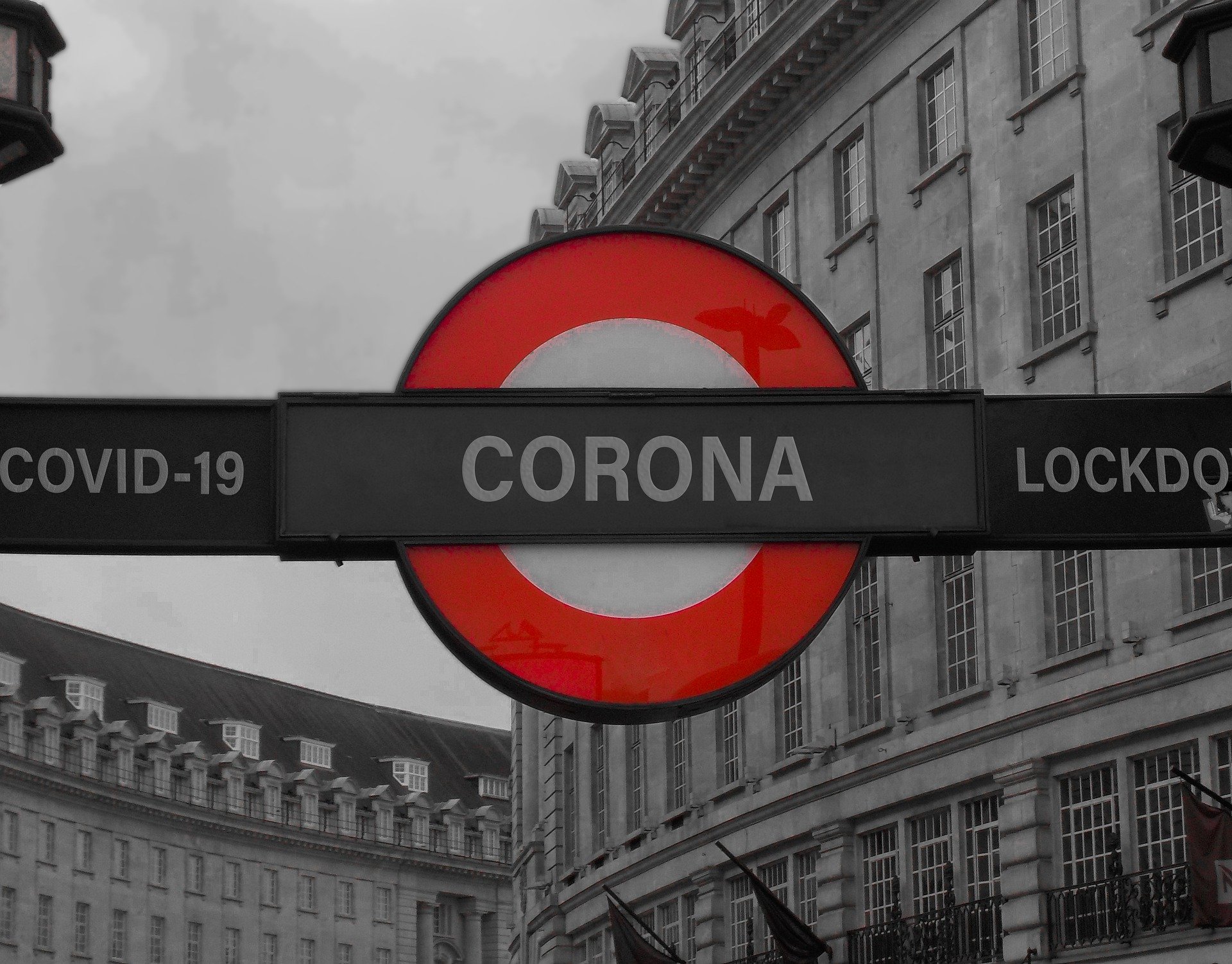 Auf einem Schild im Stil der Londoner U-Bahn steht "CORONA" mit "COVID-19" auf der linken Seite und "LOCKDOWN" auf der rechten Seite vor einem Straßenhintergrund in Graustufen.