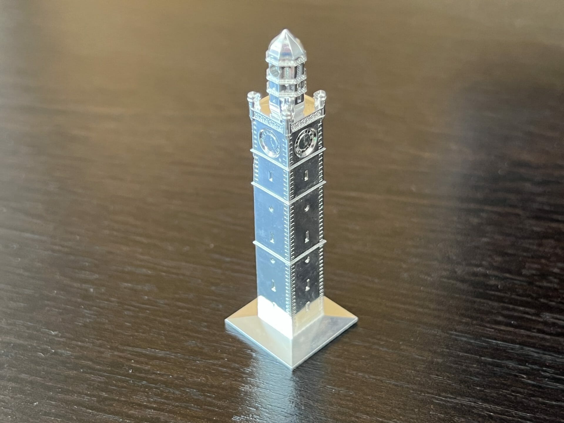 Ein kleines Metallmodell einer Turmuhr steht auf einer dunklen Holzfläche.